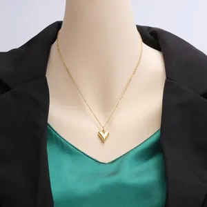 Detail shot of a minimalist gold heart pendant necklace styled with a green top