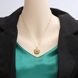 Close-up detail of a gold-plated evil eye coin pendant necklace worn with a black blazer.