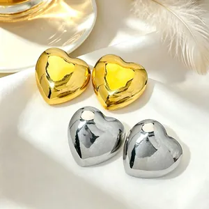 Close-up of polished gold and silver heart-shaped stud earrings on white silk fabric