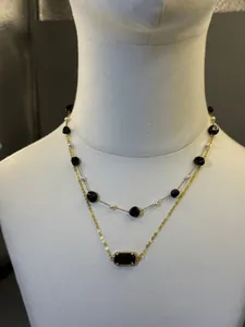 Dettaglio di una collana multistrato placcata oro 18 carati con pietre nere e perle bianche.