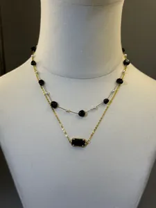 Primo piano di collana dorata a doppio strato con pietre nere e perle su manichino