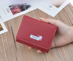 Detail close-up of a red small leather wallet featuring white stitching and a flower patch