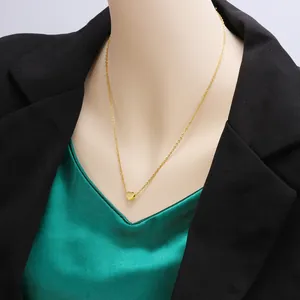 Close-up of a gold heart pendant necklace worn on a model with a black blazer.
