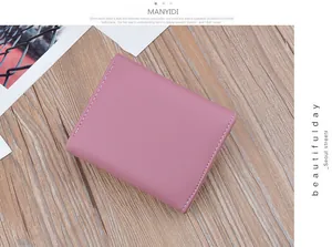 Detail view of a pink soft leather short bifold wallet on a light wooden background