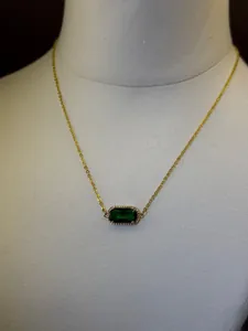 Primo piano di una collana placcata in oro con un ciondolo di pietra verde smeraldo.