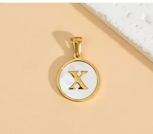 Close-up of a gold stainless steel round pendant with a white shell inlay and letter X.