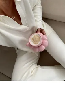 Close-up of pink flower-shaped ceramic coffee cup set in a cozy lifestyle setting.
