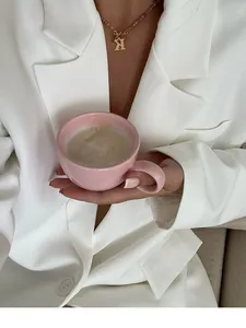 Detail view of a pink luxury ceramic coffee cup held by a model in a white blazer.