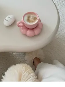 Close-up detail of a pink flower-shaped ceramic coffee cup set on a white table