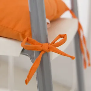 Close-up of a vibrant orange solid color chair cushion with functional tie on a gray metal chair
