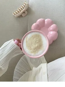 Top view detail of a pink flower-shaped coffee cup with foam on a beige background