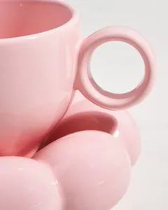 Detail view of a pink ceramic coffee cup with petal-shaped saucer and round handle