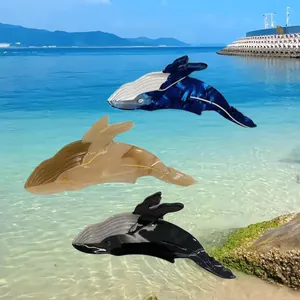 Mollette per capelli in acetato a forma di balena in blu, marrone e nero su una spiaggia.