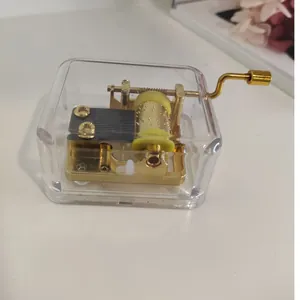 Detalle de una caja de música transparente de manivela con movimiento mecánico dorado