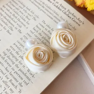 Detail eleganter cremefarbener Stoffrosen-Haarspangen mit weißen Perlen auf einem Buch.