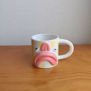 Creative blobfish face ceramic coffee mug with yellow stripes on a wooden desk surface