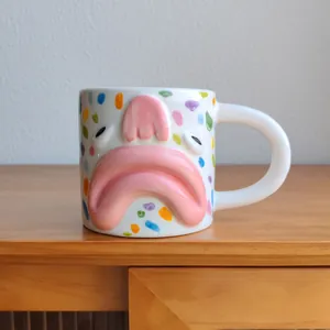 Close-up detail of a creative sad face ceramic coffee mug with colorful polka dots design