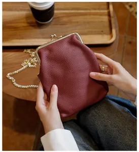 Detail of a burgundy pebbled leather phone bag with a gold chain strap held by hands.