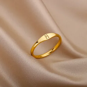 Detailed view of a gold minimalist ring with an engraved letter H on silk fabric