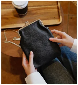 Detailed view of hands holding a black genuine leather kiss-lock phone bag with chain