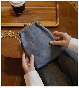 Close-up of a grey textured leather phone bag with metal clasp held in a cozy cafe setting