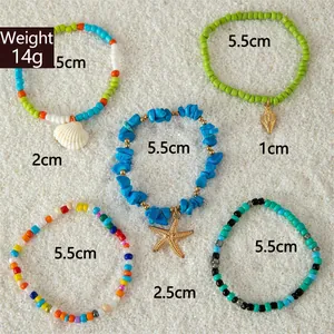 Detailweergave van vijf bohemian kralenarmbanden met strandbedels op fijn wit zand
