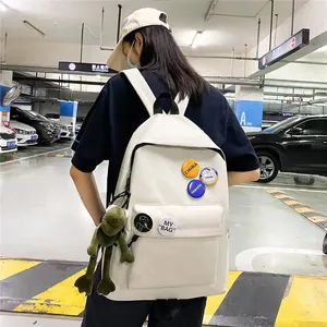 Vue arrière d'un sac à dos blanc avec pendentif grenouille et badges dans un parking.