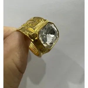 Close-up detail of a men's gold alloy ring featuring a large square clear gemstone.