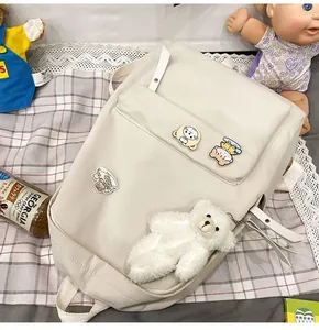 Dettaglio dello zaino in tela beige minimalista con spille carine e ciondolo orsetto plush