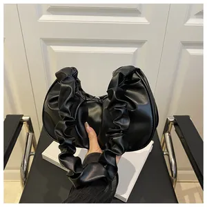 Dettaglio di una borsa a nuvola nera plissettata minimalista con manico arricciato.