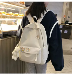 Zaino minimalista beige con badge a cartoni animati e ciondolo a forma di orsetto.