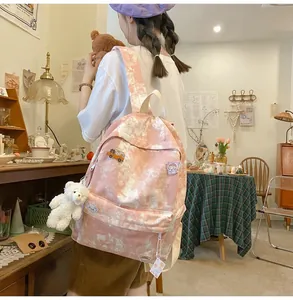 Pink tie-dye backpack for students featuring a cute plush bear charm and decorative pins.