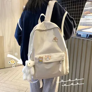 Primo piano di uno zaino crema minimalista con spille carine e portachiavi orso
