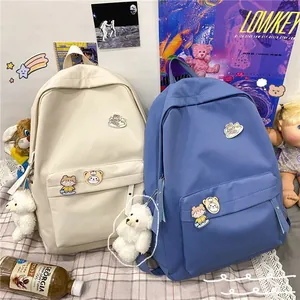 Primo piano di zaini stile Harajuku in tinta unita con spillette e ciondoli a orsetto.