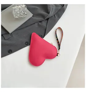 Détail d'un sac à main rose en forme de cœur avec une dragonne imprimée.