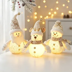 Three glowing Christmas dolls Santa reindeer snowman on tabletop with warm lights