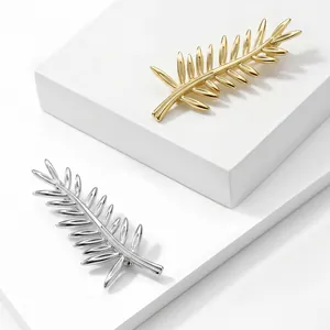 Detailed close-up of elegant gold and silver leaf brooches on white tiered display blocks