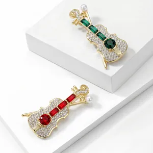 Dettaglio di eleganti spille a forma di violino con pietre rosse e verdi brillanti.