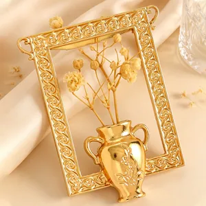 Nahaufnahme einer goldenen Vintage-Brosche mit Vasen-Rahmen-Design und Trockenblumen