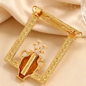 Detailansicht einer goldfarbenen Blumenstrauß-Brosche mit Vasendesign auf Seide.