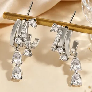 Close-up of irregular silver hoop earrings with dangling pear-shaped zircons