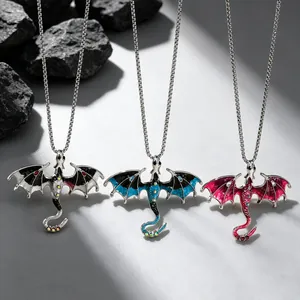 Three gothic dragon pendant necklaces in blue, pink, and black colors on rocks.
