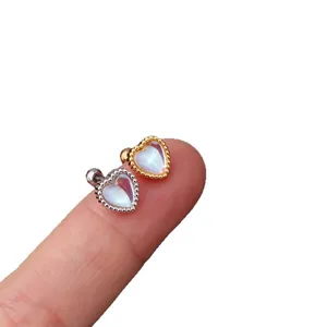 Elegant heart-shaped moonstone cartilage studs in silver and gold finish on a finger.