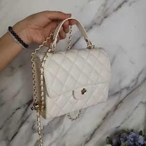 Detailed view of white quilted mini handbag with gold chain strap and floral clasp.