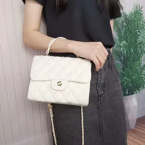 Close-up of white quilted flap bag with golden flower clasp and chain strap.