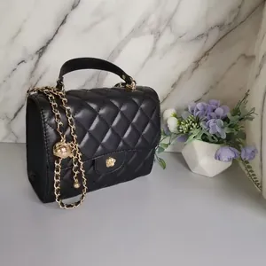 Close-up detail of black quilted mini handbag with gold chain strap on a marble background