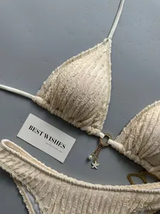 Detailed close-up of cream textured bikini set with gold hardware and pearl charms