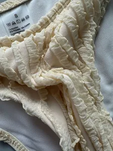 Close-up of cream textured fabric and care label on a ruffled bikini swim bottom
