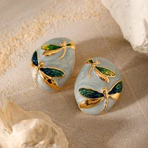 Elegant oval enamel earrings with golden dragonfly motifs on a textured stone background