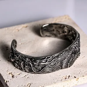 Detailed view of an antique-finish stainless steel cuff bracelet with dragon carvings.